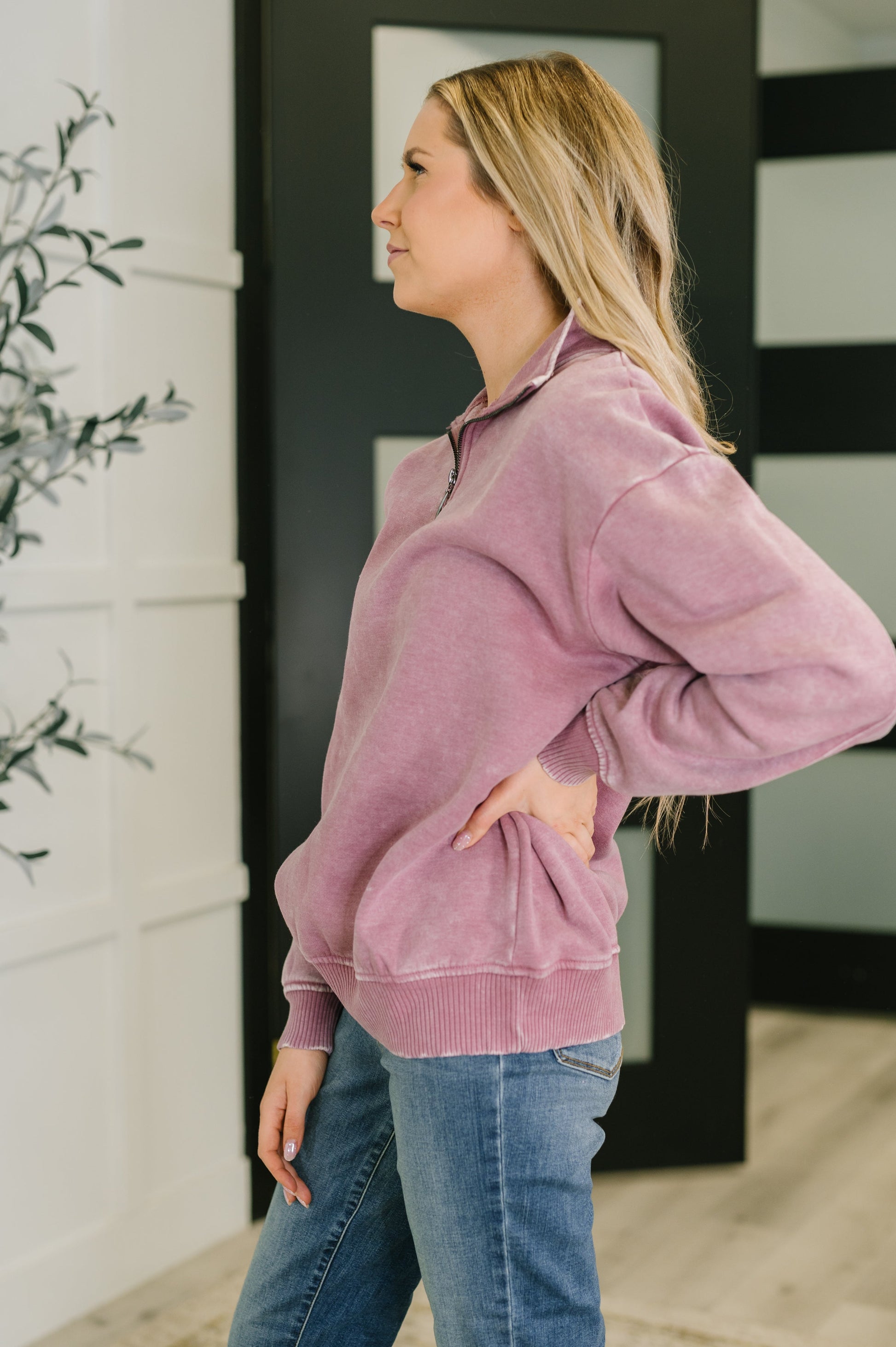 Woman wearing a pink pullover and blue jeans indoors.
