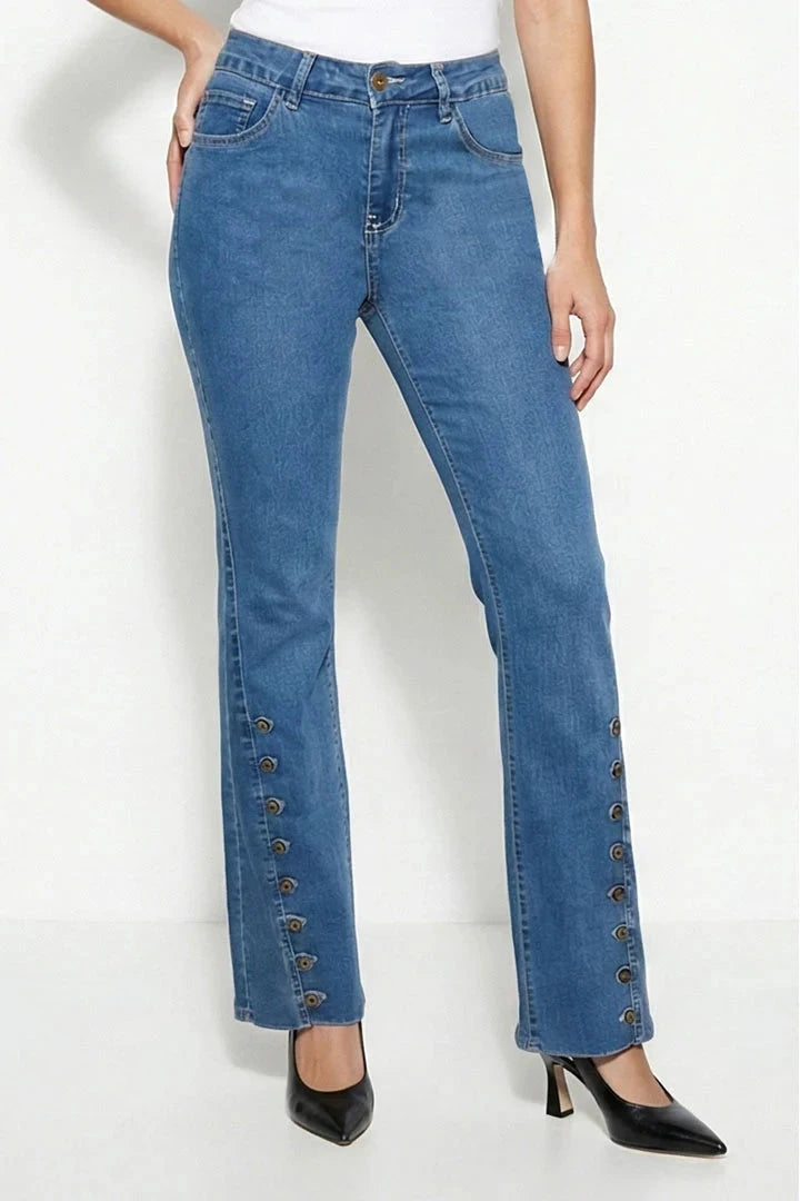 A model wearing blue denim jeans with decorative metallic button details running down the outer sides of the legs, paired with a white top and black pointed-toe heels.
