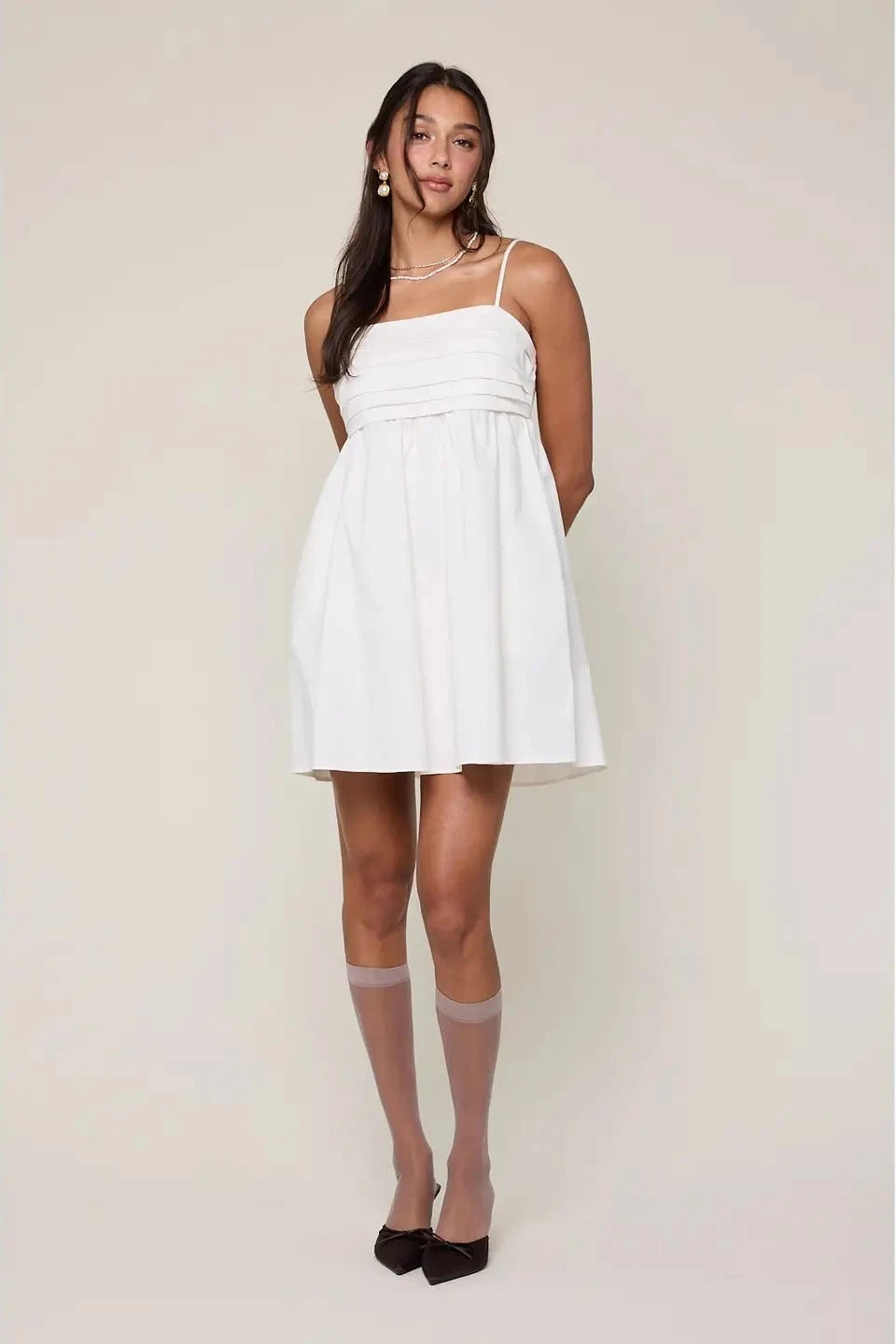 Woman wearing a white dress with sheer stockings against a plain background