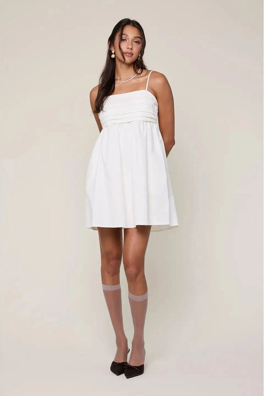 Woman wearing a white dress with sheer stockings against a plain background
