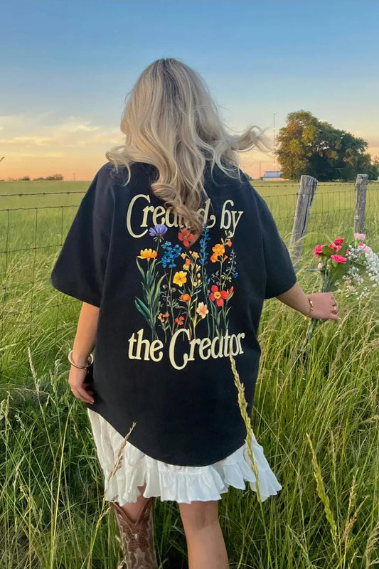 Person wearing a black t-shirt with floral design and text in a field