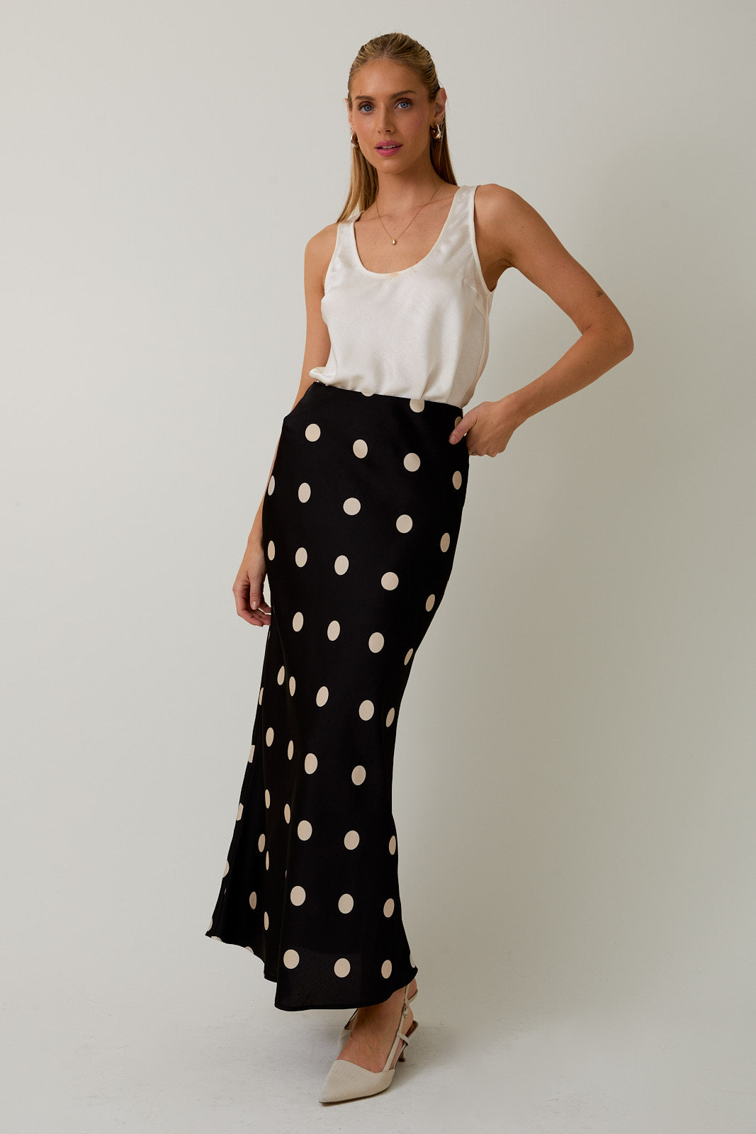 Woman wearing a white sleeveless top and black polka dot pants on a plain background