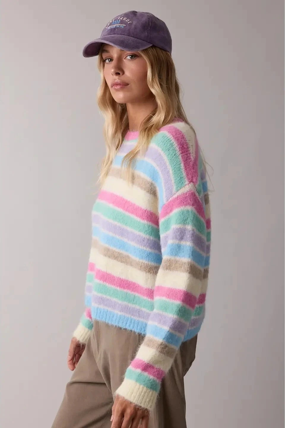 Person wearing a colorful striped sweater and purple cap on a plain background