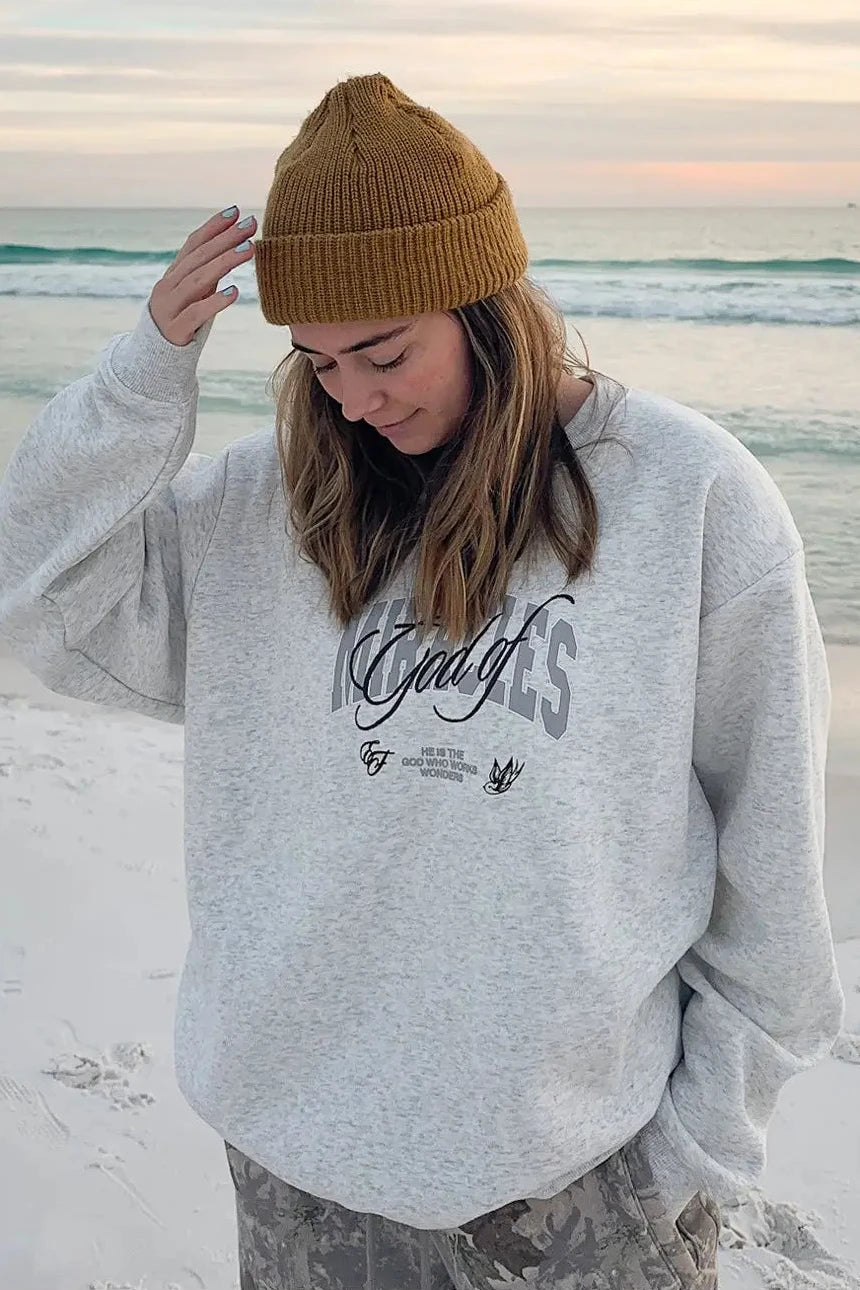 Person wearing a gray sweatshirt with text on a beach at sunset