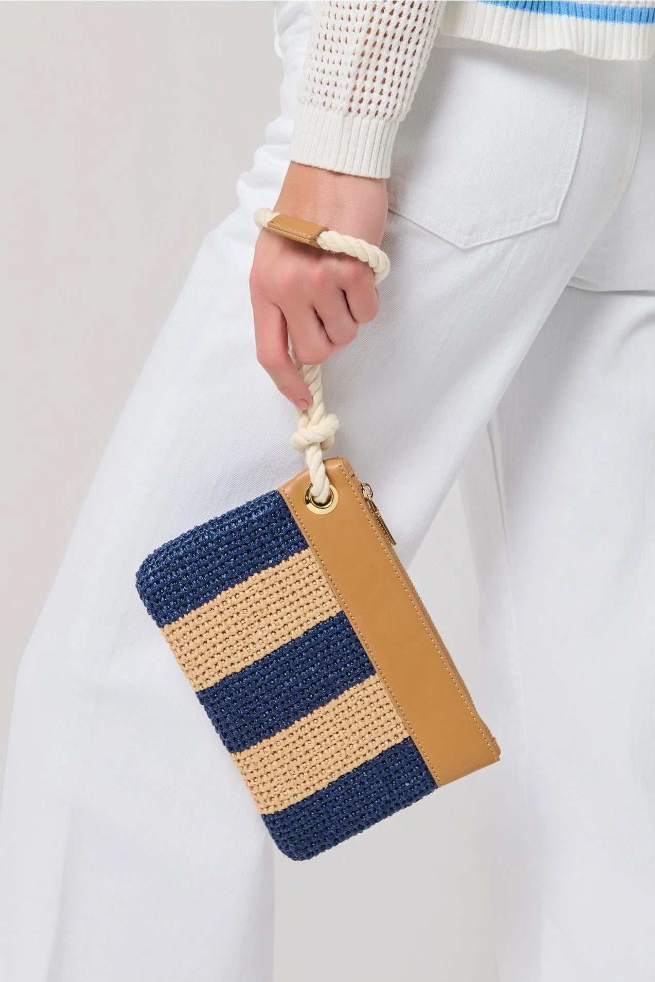 Hand holding a striped clutch bag with blue and brown colors against a plain background