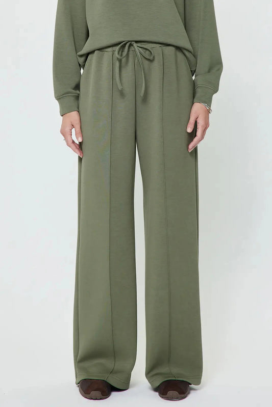A person wearing olive green wide-leg drawstring pants with a matching long-sleeve top, shown from the chest down against a plain light gray studio background.