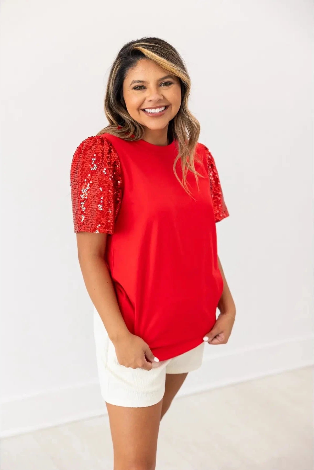 Woman wearing a red top with sequin sleeves on a white background