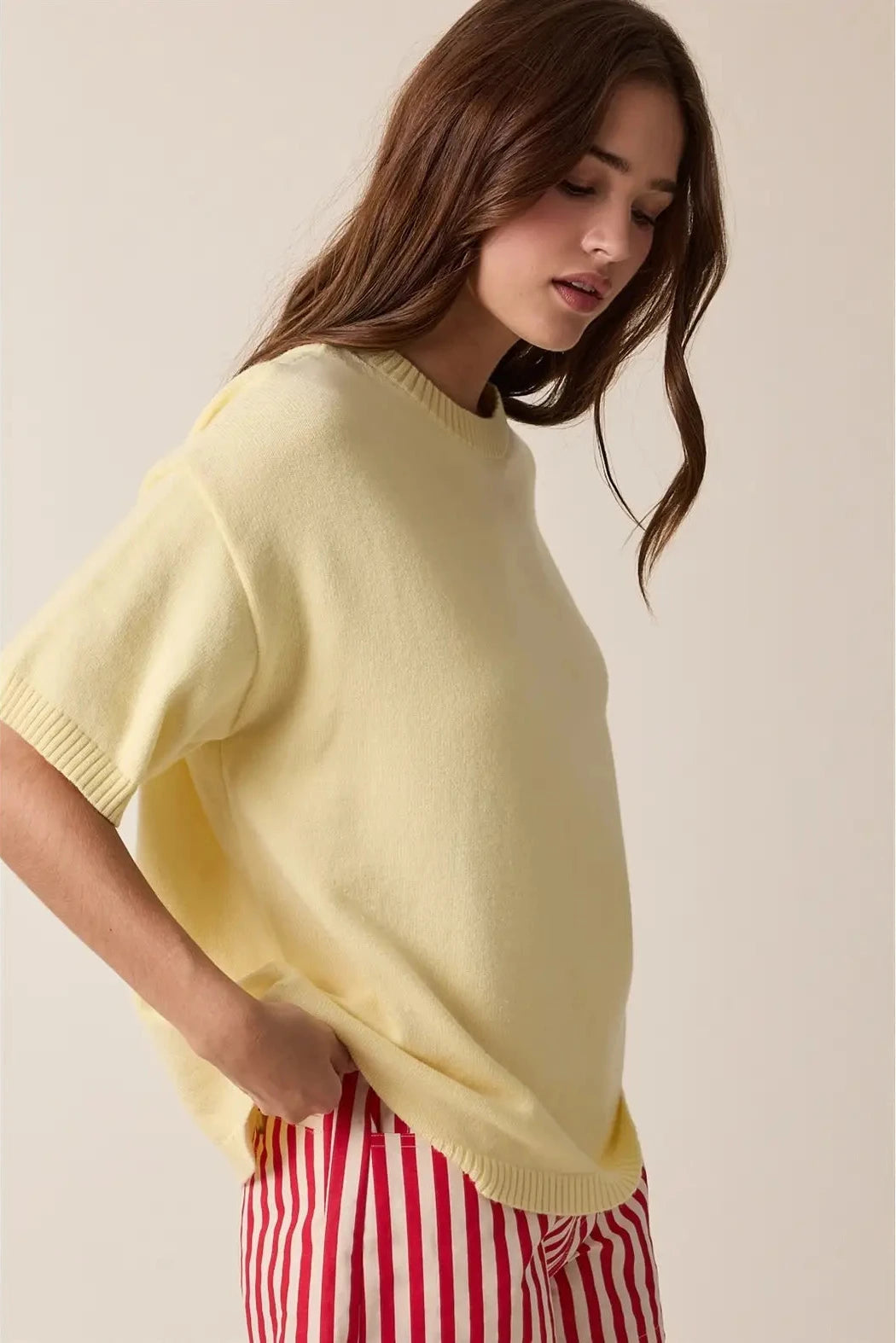 Woman wearing a light yellow sweater and red striped pants against a beige background