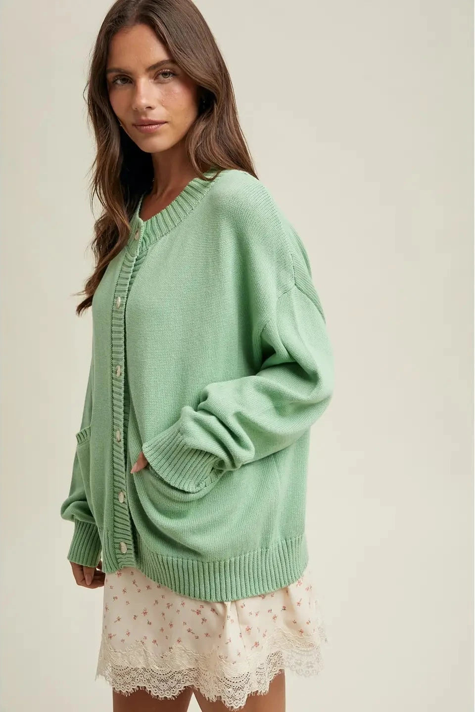 Woman wearing a light green cardigan over a white lace dress on a plain background