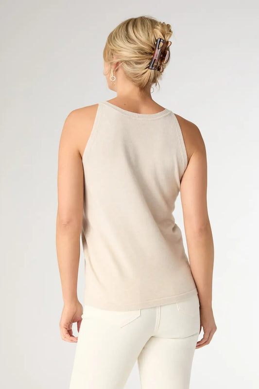 Woman wearing a beige sleeveless top and white pants on a plain background