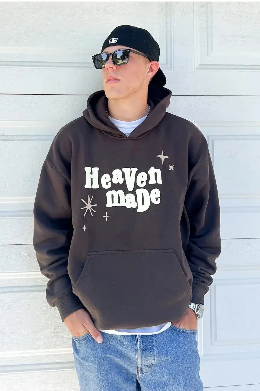 Person wearing a dark hoodie with 'Heaven made' text, standing against a white wall.