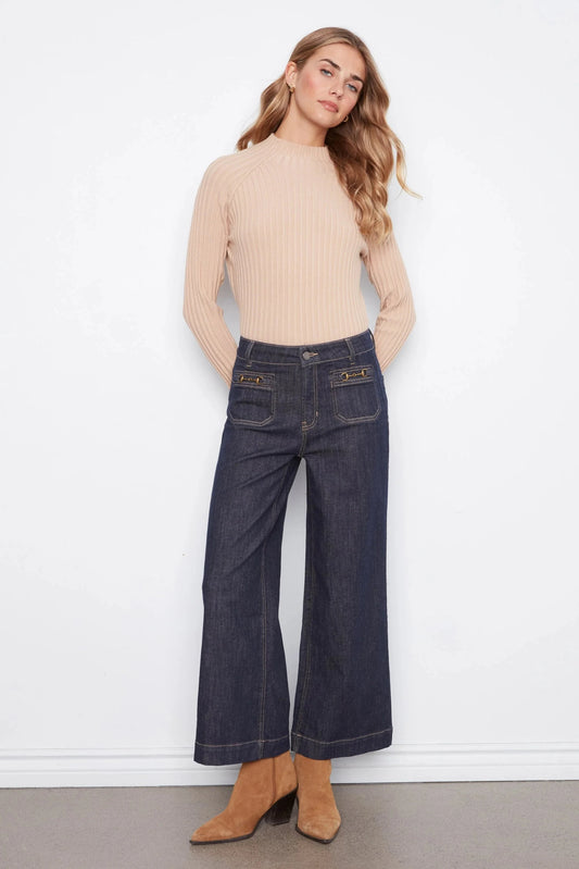 Woman wearing a beige sweater and dark blue jeans against a white background