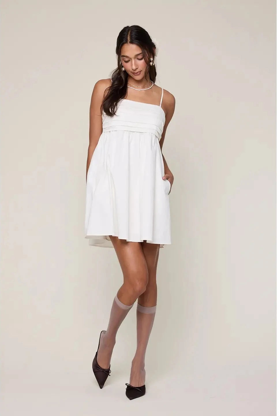 Woman wearing a white dress with black high-heeled shoes on a plain background