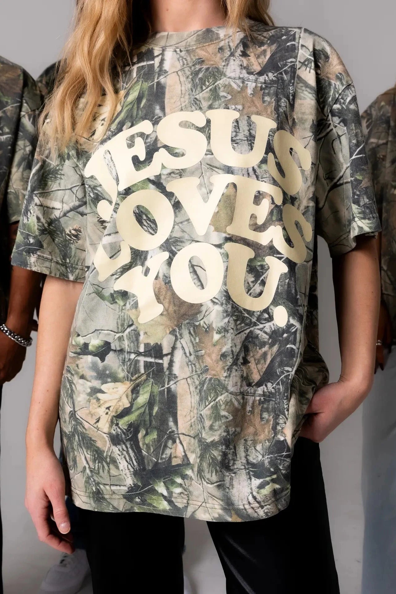 Person wearing a camouflage t-shirt with 'Jesus Loves You' text.