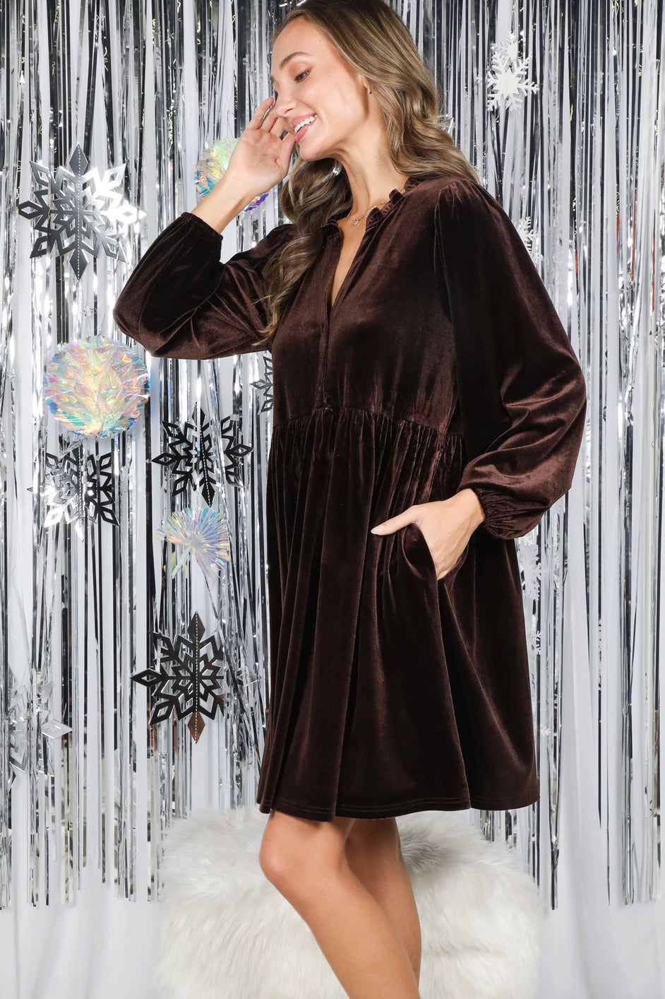Woman wearing a brown velvet dress against a decorative silver curtain background