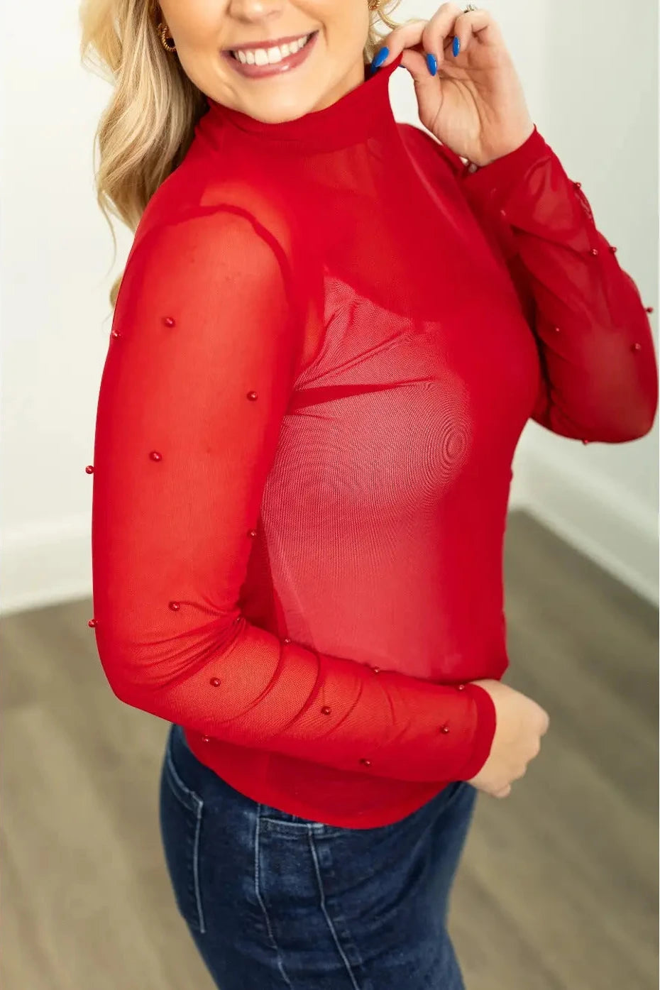 Woman wearing a red long-sleeve top with beaded details against a neutral background