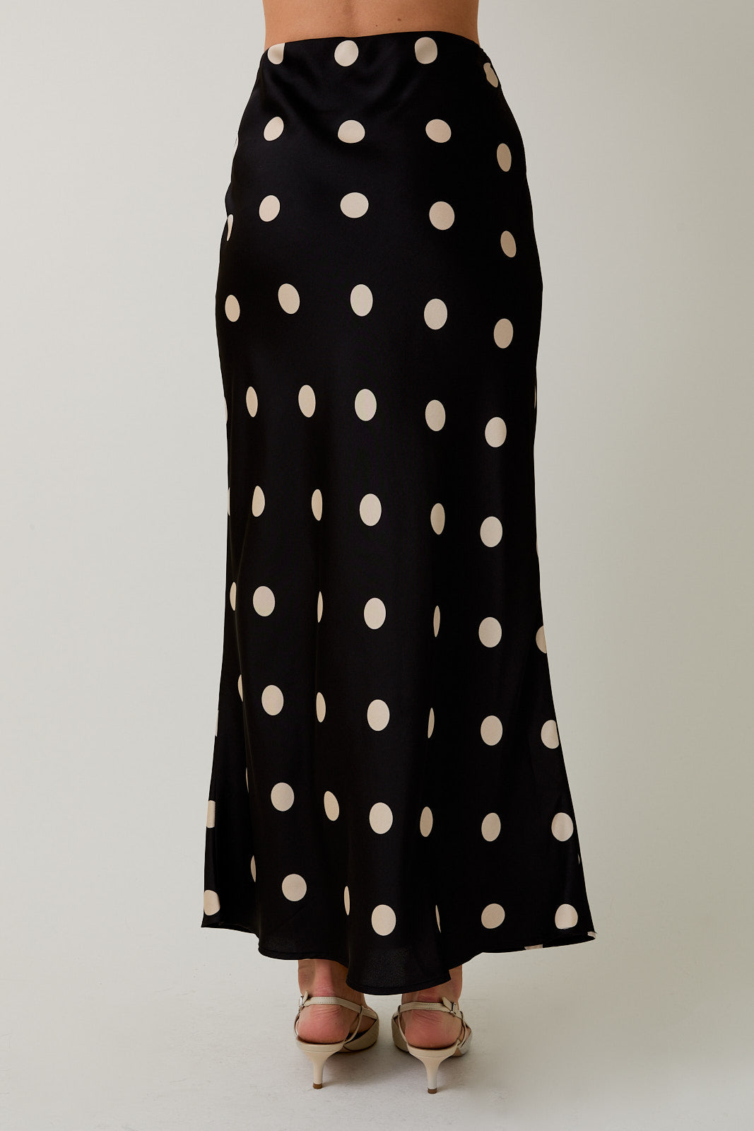 Black skirt with white polka dots worn by a person on a plain background