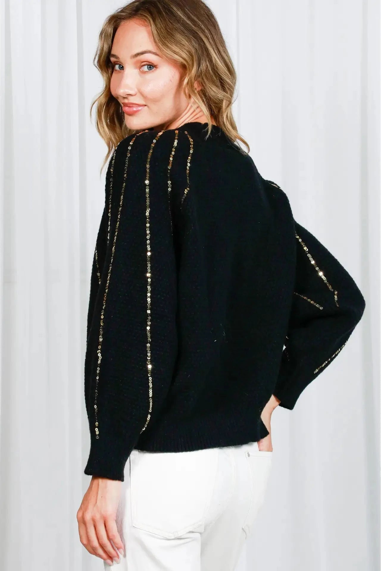 Woman wearing a black sweater with gold accents against a white background