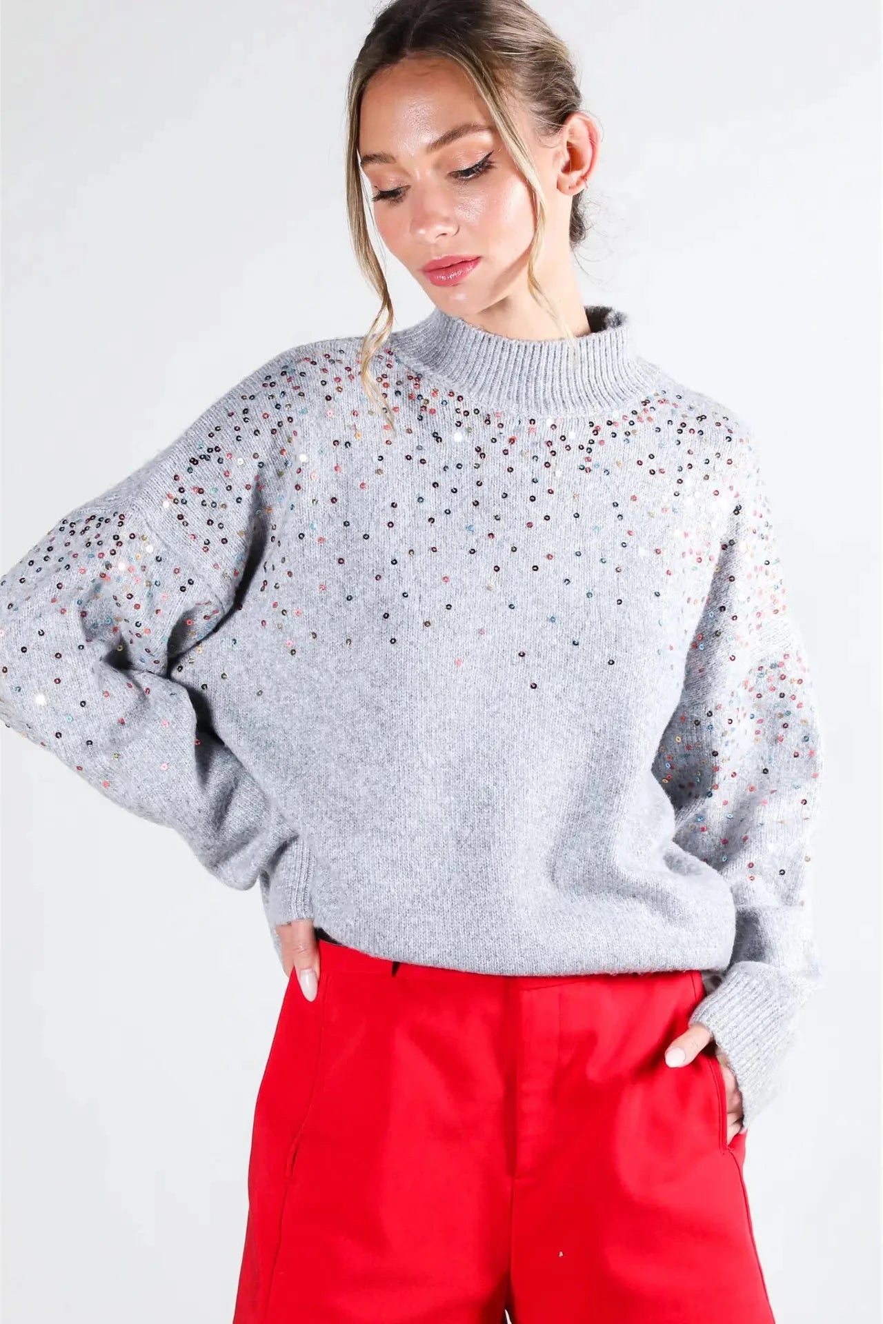 Woman wearing a gray sweater with star patterns and red pants on a white background