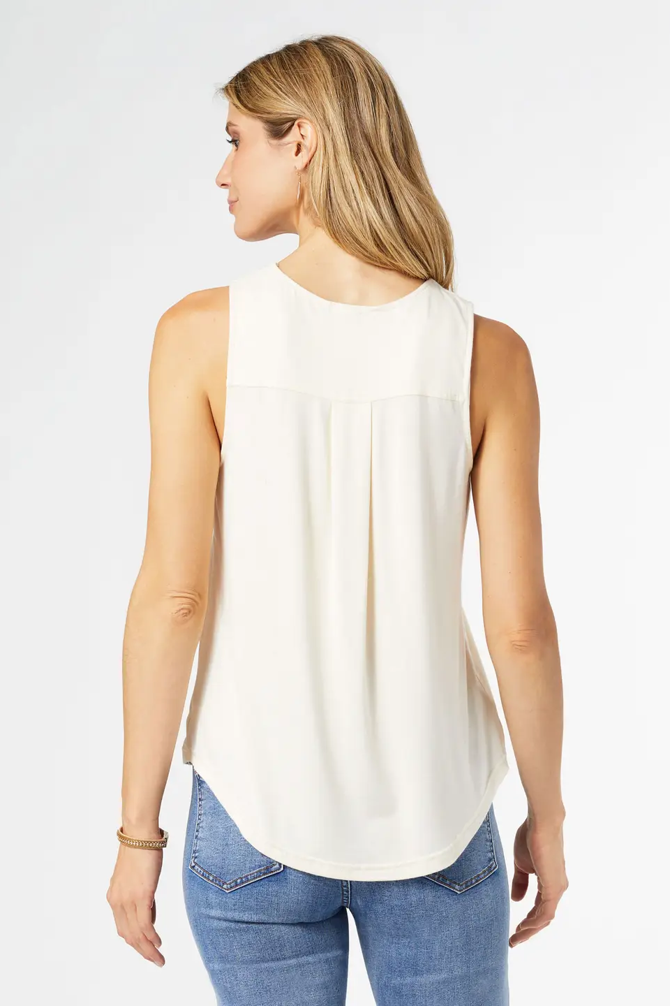 Woman wearing a white sleeveless top and blue jeans on a plain background