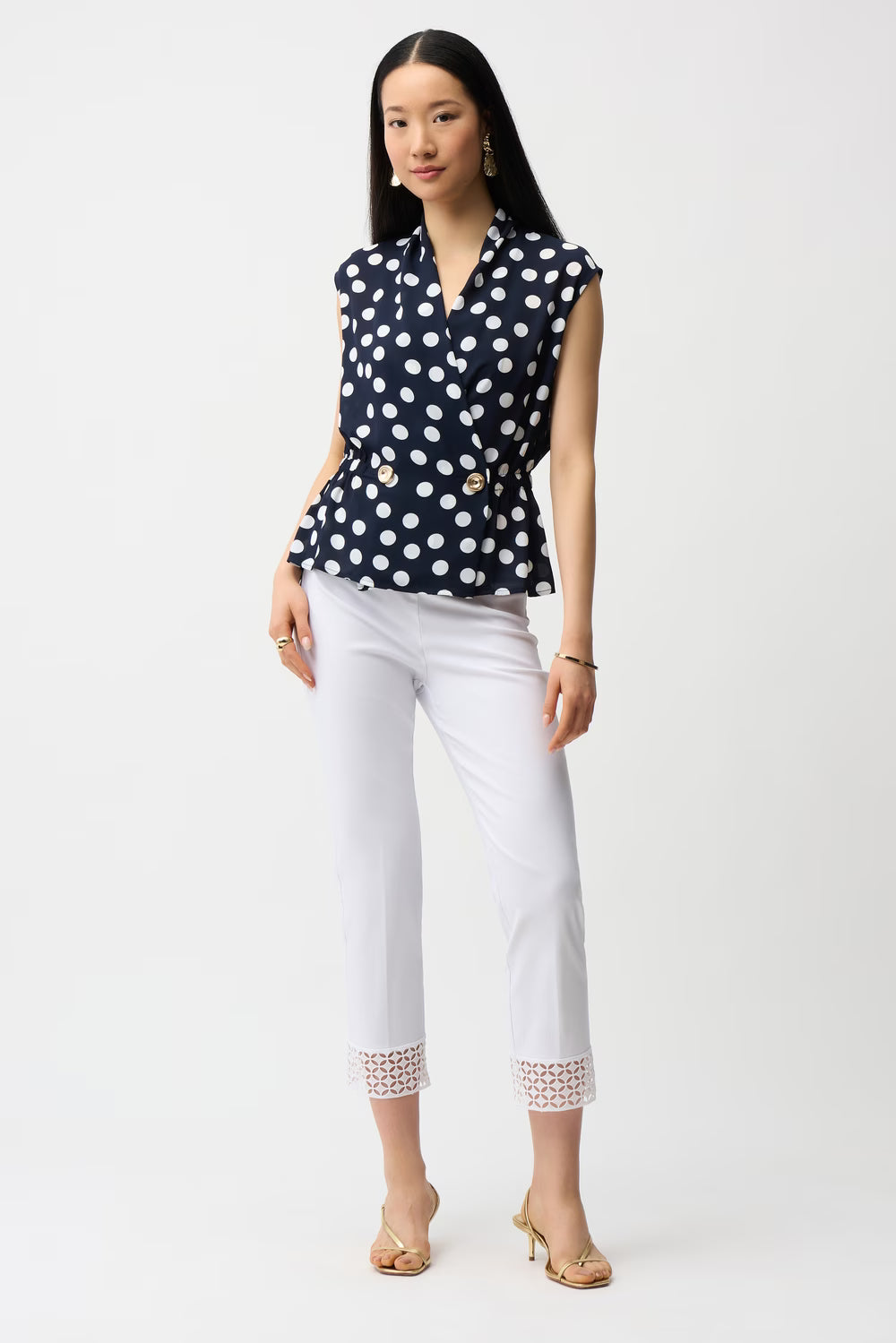 Woman wearing a navy blue top with white polka dots and white pants on a white background