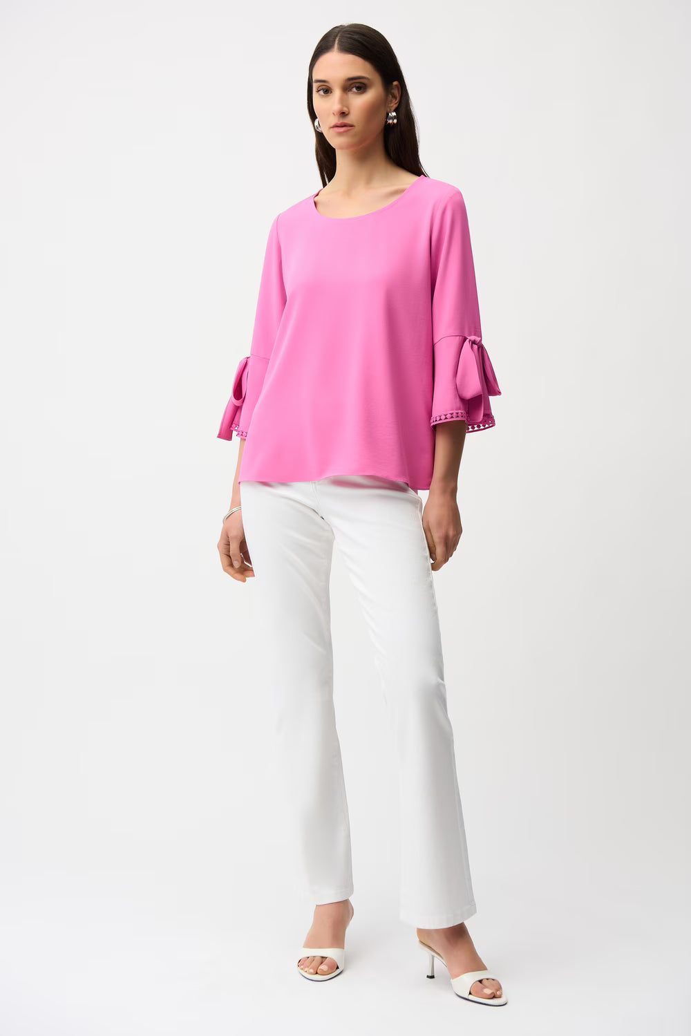 Woman wearing a pink blouse with bell sleeves and white pants on a white background