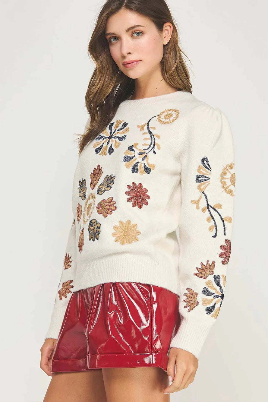 Woman wearing a white sweater with floral patterns and a red skirt on a white background